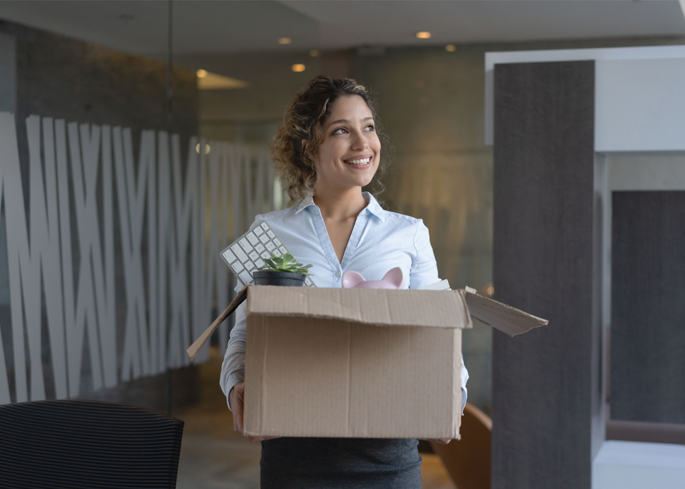 Person smiling carrying a cardboard box of their work items out of an office
